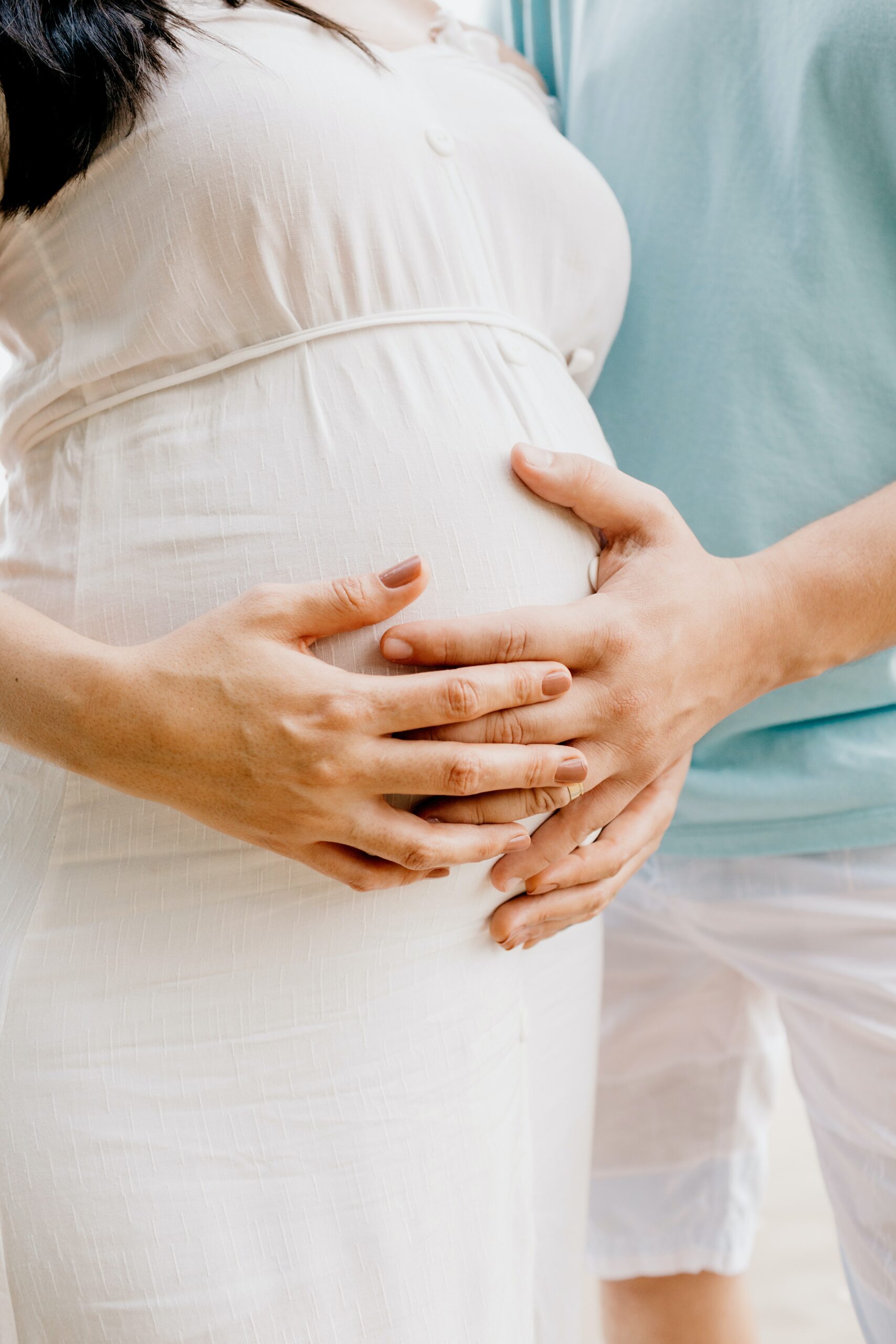 Pregnant women that is newly diagnosed with gestational diabetes in white dress holding stomach standing next to man in blue shirt.